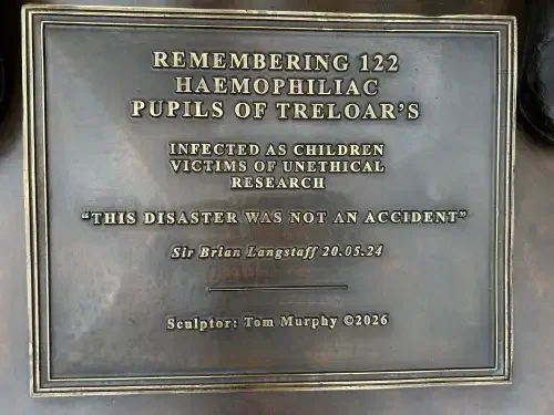 Bronze plaque on the memorial reading: Remembering 122 haemophiliac pupils of Treloar's. Infected as children. Victims of unethical research. This disaster was not an accident, Sir Brian Langstaff, 20.05.24. Sculptor: Tom Murphy 2026.
